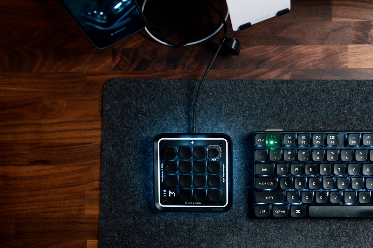 A stylish office desk setup with keyboard, MIDI controller, and smartphone on a dark wooden table.